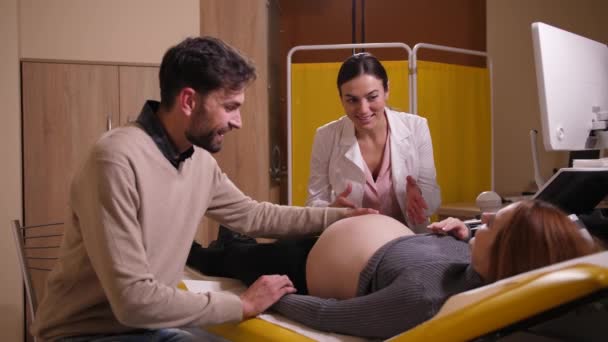 Счастливый мужчина гладит беременную жену животом в клинике
 - Кадры, видео