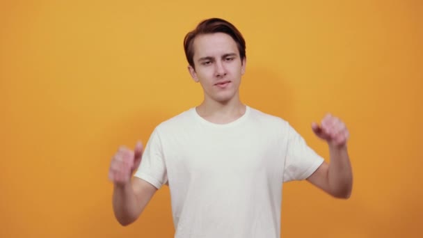 Young man in white t-shirt puts his hands behind head on yellow background. - Footage, Video
