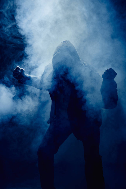 fist and hand of a man in a leather jacket and hoodie in mist against the light - Foto, Bild