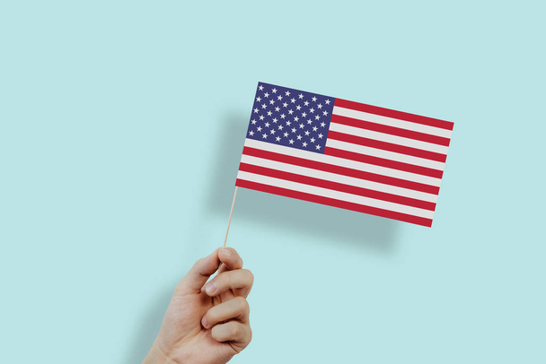 The US flag held in hands. The hand lifts the flag of the United States on a green, pastel background. The concept of citizens, independence, love for their country. Patriotism. - Φωτογραφία, εικόνα