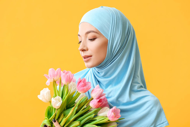 Beautiful Muslim woman with flowers on color background. International Women's Day celebration - Photo, Image