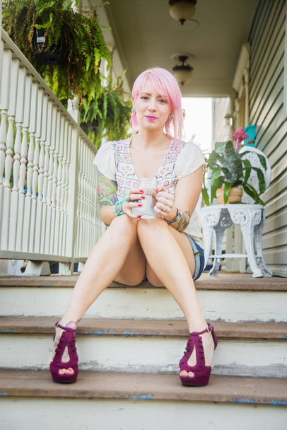 Portrait of young woman with pink hair sitting on porch steps - 写真・画像