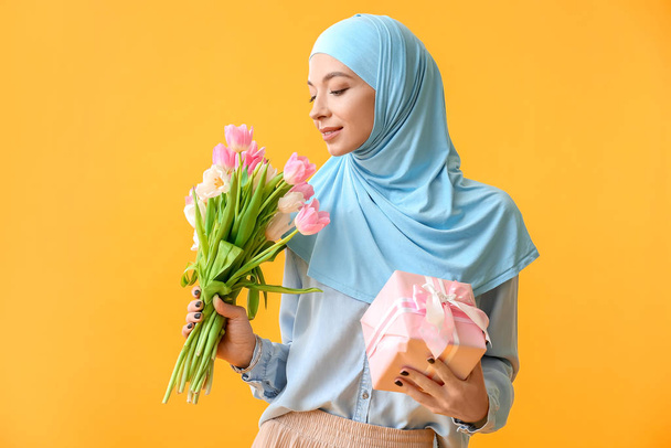 Krásná muslimská žena s květinami a dárek na barevném pozadí. Mezinárodní oslava Dne žen - Fotografie, Obrázek