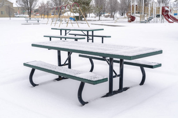 Tavoli da picnic innevati e panchine in un parco coperto di neve in inverno
 - Foto, immagini