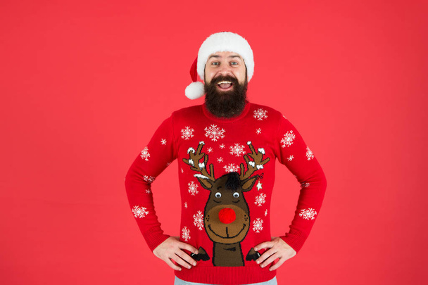 cheerful hipster funny knitted sweater. warm clothes in cold winter weather. holiday season mood. bearded man santa hat red background. merry christmas. ready for xmas party. happy new year - Foto, Imagen