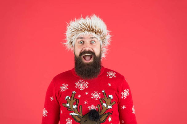 celebración de vacaciones de invierno. moda de clima frío para los hombres. Feliz año nuevo. hombre barbudo sonriendo sobre fondo rojo. un hombre divertido con barba en jersey de punto. hipster sorprendido listo para fiesta de Navidad - Foto, imagen