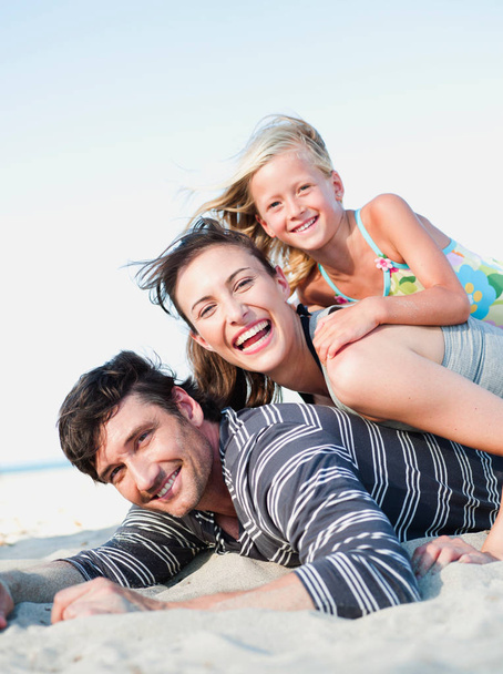 family lying in sand on beach smiling - Fotó, kép