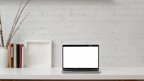 Vista ravvicinata del computer portatile dello schermo vuoto, modello su telaio, libri e decorazioni su tavolo bianco con sfondo muro di mattoni
    - Foto, immagini