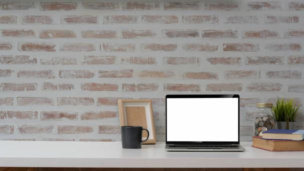 Gesneden schot van blanco scherm laptop, mock up frame en decoraties op witte tafel met bakstenen muur achtergrond    - Foto, afbeelding