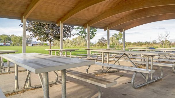 Marco panorámico Zona de comedor en un parque con mesas y asientos bajo techo de madera marrón del pabellón
 - Foto, imagen
