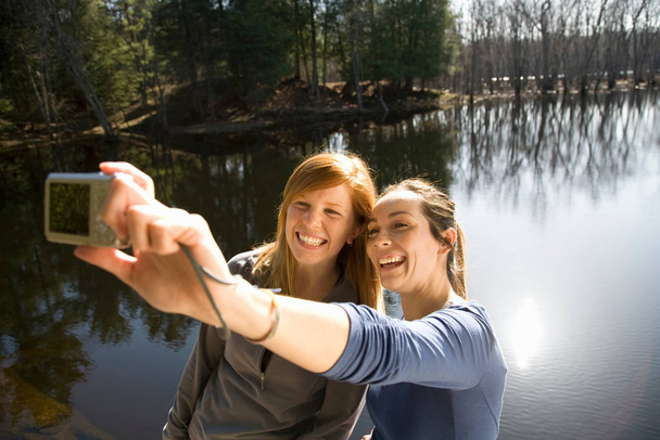 Two women with camera beside lake - Фото, зображення