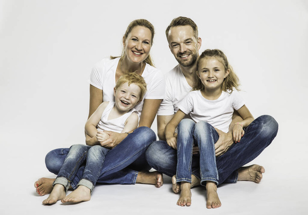 Studio portrait of boy and girl with mature parents sitting on floor - Фото, изображение