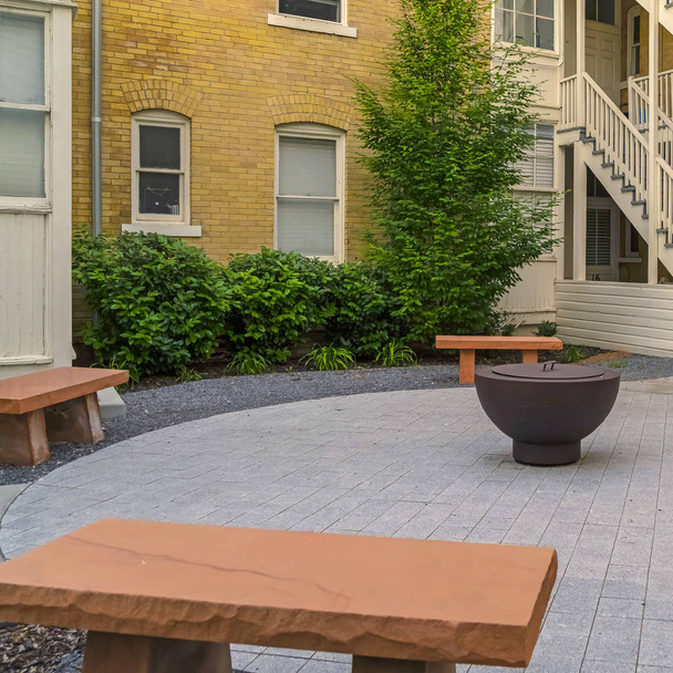 Square frame Fire pit on circular pavement with stone benches against building exterior - Photo, Image