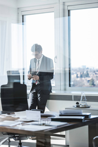 Businessman standing in office using smartphone - Фото, зображення