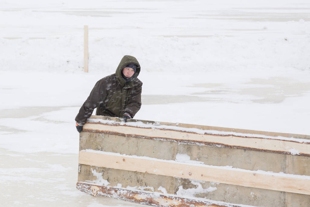 Працівник в зимовому комбінезоні тягне дерев'яний щит
 - Фото, зображення