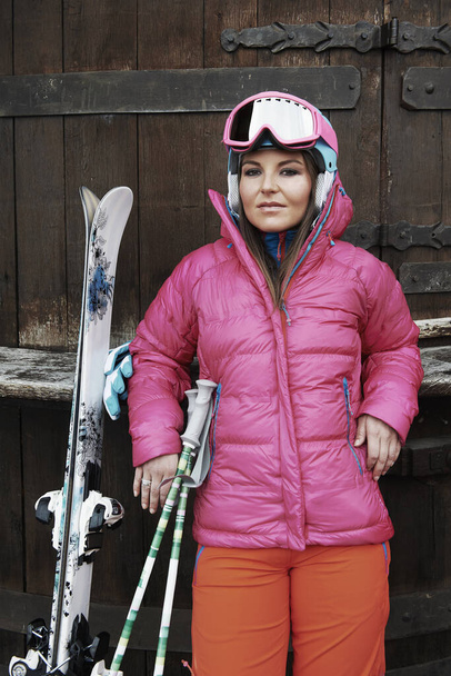Young woman leaning against door, wearing skiwear and carrying ski equipment - Fotó, kép