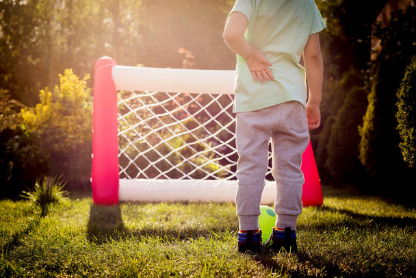 A forward view on goal on a boy's kicking ball. The boy is playing ball, he is kicking the ball straight to the goal. The child in action plays soccer. Shared time with family. - Foto, Imagen