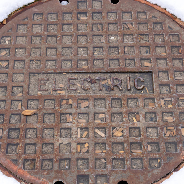 Square frame Rusty circular utility electric manhole cover amid fresh white snow in winter - Photo, Image