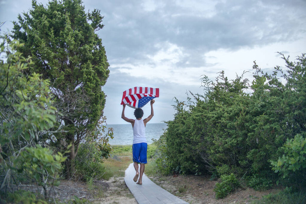 Rear view of boy holding up American flag on coastal path, Cape Cod, Massachusetts, USA - Valokuva, kuva
