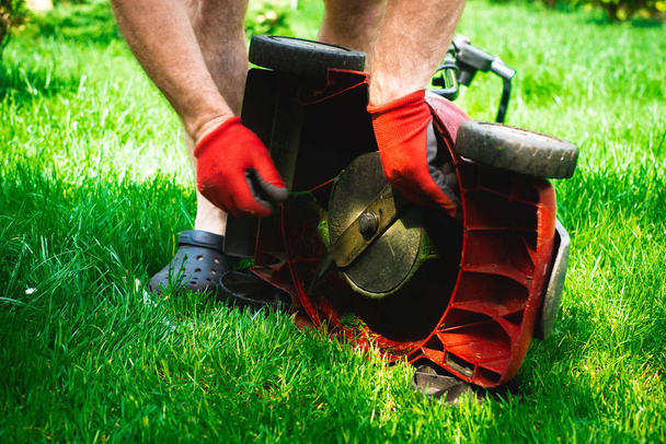 Man exchanges the mower's knife with a new one. Mowing the grass. Gardener mows the grass with a red electric mower. Work in the garden, spring cleaning. Care for the garden and grass. - Photo, Image