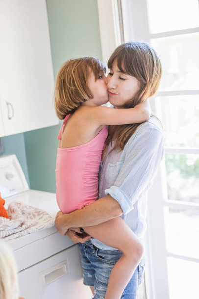 Mother and daughter hugging in utility room, portrait - Foto, afbeelding
