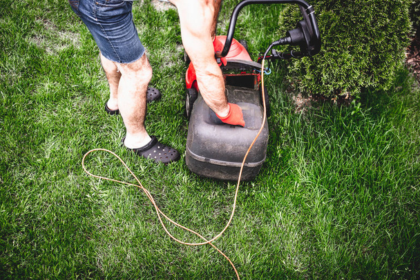 Vue de dessus sur la tonte de l'herbe. Le jardinier tond l'herbe avec une tondeuse électrique rouge. Travail dans le jardin, nettoyage printanier. Entretien du jardin et de l'herbe
. - Photo, image