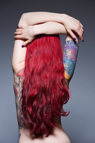 Young woman with long red hair and tattoos, studio shot - Foto, Imagen