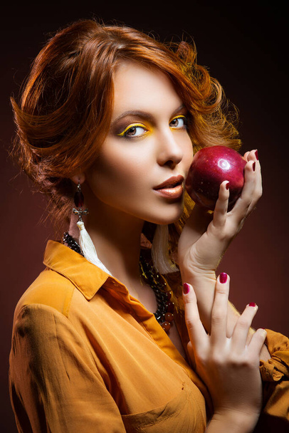 Beautiful young woman with bright yellow makeup dressed in orange autumn style holding red apple - Foto, imagen