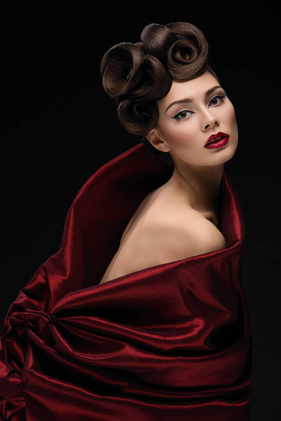Όμορφη νεαρή γυναίκα με μοντέρνο χτένισμα και μακιγιάζ σε κόκκινο ύφασμα που μοιάζει με τουλίπα - Φωτογραφία, εικόνα