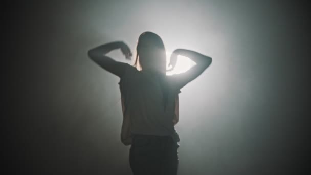 Una silhouette di donna che balla con le mani sullo sfondo di un'illuminazione luminosa
 - Filmati, video