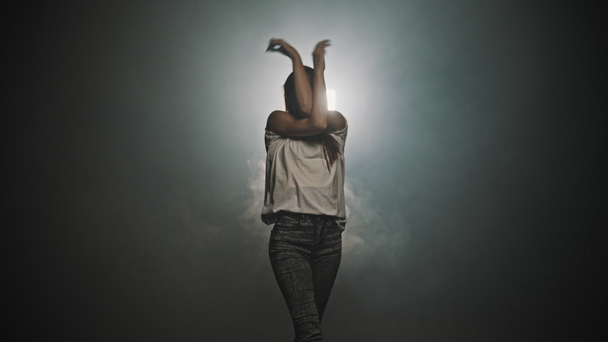 Een silhouet van jonge vrouw dansend met haar handen op de achtergrond van helder licht - lopend uit het donker - Video