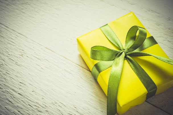 Present for Mother's day, Valentine's or birthday. Gift box wrapped in yellow paper with a green ribbon on white wooden background. Vintage Style. Toned Image. Copy space. Selective focus. - 写真・画像