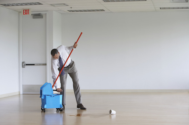 Businessman using mop in empty room - Foto, afbeelding