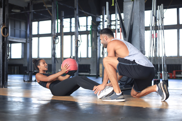 Тренер помогает молодой женщине делать упражнения для брюшной полости в спортзале. - Фото, изображение