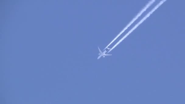 Beyaz bir yolcu uçağı gökyüzünde yükseklerde uçar ardında bir yoğunluk, ters dönüş ve jet izi bırakır. - Video, Çekim
