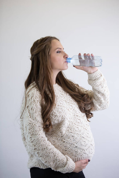 Pregnant girl drinks water from a bottle and holds her belly with her hand. - Φωτογραφία, εικόνα