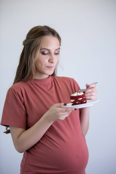 A pregnant girl in a pink T-shirt looks at the cake and wants to eat it. - Φωτογραφία, εικόνα