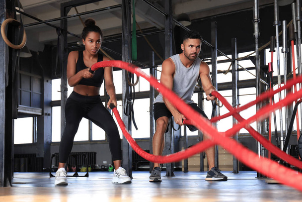 Athletic young couple with battle rope doing exercise in functional training fitness gym. - Valokuva, kuva