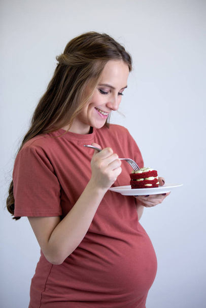 A pregnant girl in a pink T-shirt looks at the cake and wants to eat it. - Foto, Imagen