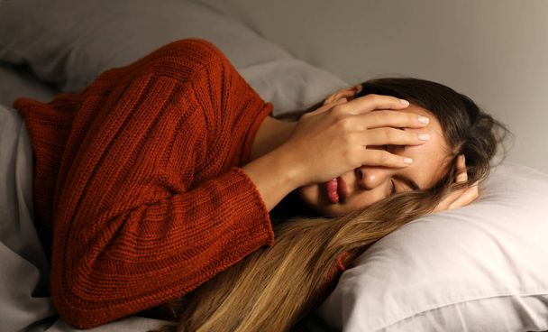Jonge vrouw heeft moeite om in slaap te vallen. Meisje met slapeloosheid of hoofdpijn bedek haar gezicht met de hand. - Foto, afbeelding
