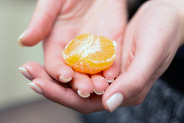 La ragazza tiene in mano un pezzo di mandarino. Mani di una ragazza
 - Foto, immagini