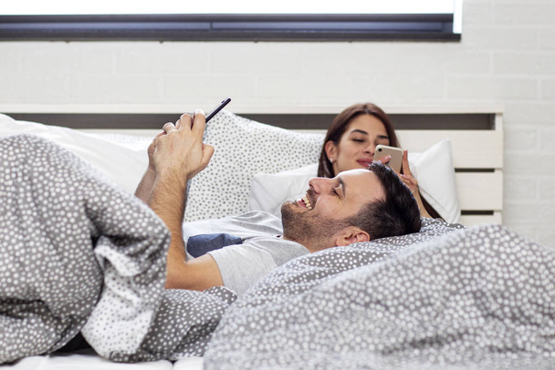 Couple in bed with electronic devices in morning - Photo, image