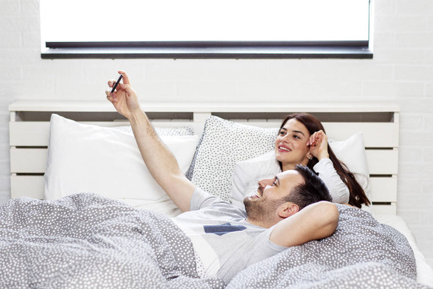 Pár v posteli s elektronickým zařízením v dopoledních hodinách - Fotografie, Obrázek
