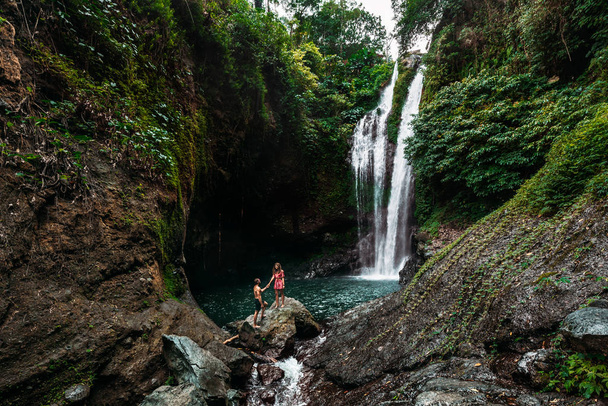 Чоловік тримає за руку гарну жінку біля водоспаду. Пара закоханих на водоспаді. Поїздка на медовий місяць. Щаслива пара на острові Балі. Красива пара подорожує світом. Подорож до Індонезії - Фото, зображення