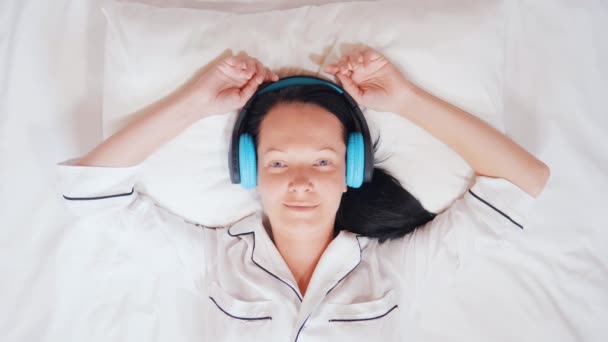 幸せな白人のブルネットはベッドの中で歌を聞く - 映像、動画