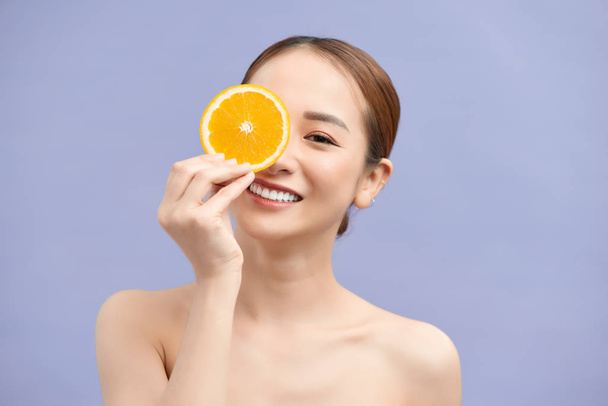 Great food for a healthy lifestyle. Beautiful young shirtless woman holding piece of orange in front of her eye while standing against white background - Photo, image