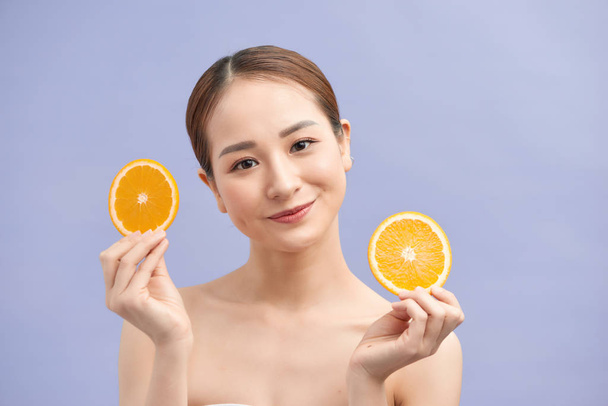 Amusante frisse aziatische vrouw met twee sinaasappels plakjes op violette achtergrond - Foto, afbeelding