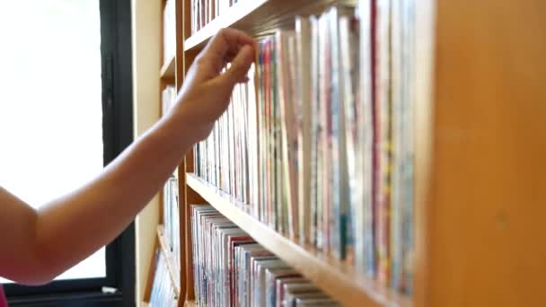 Frau sucht Bücher und holt ein Buch aus dem Bücherregal der Bibliothek. Bildungsaktivität und Lifestylekonzepte. - Filmmaterial, Video