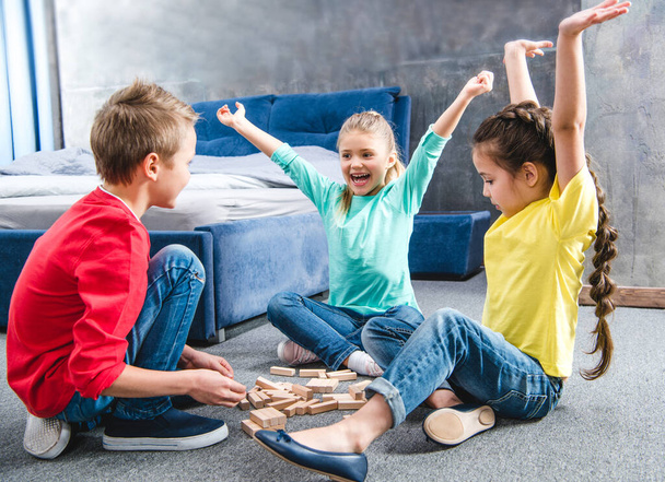 Mutlu çocuklar halıda oturup tahta bloklarla oynuyorlar. - Fotoğraf, Görsel