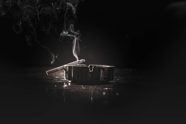 Closeup of cigarette on ashtray with a beautiful wisp of smoke  - Photo, Image